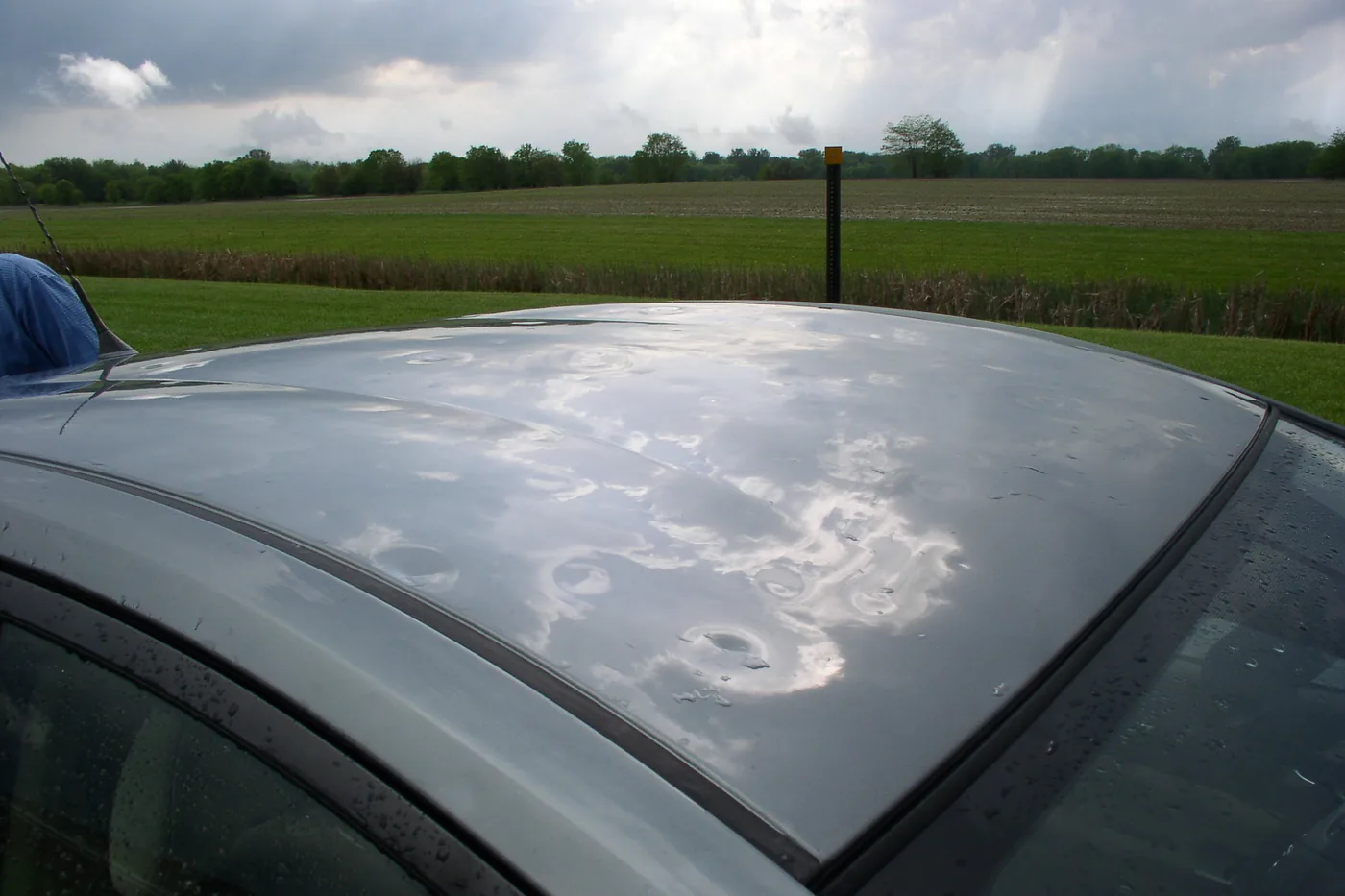 Hail dents across the roof of a silver car after a hailstorm