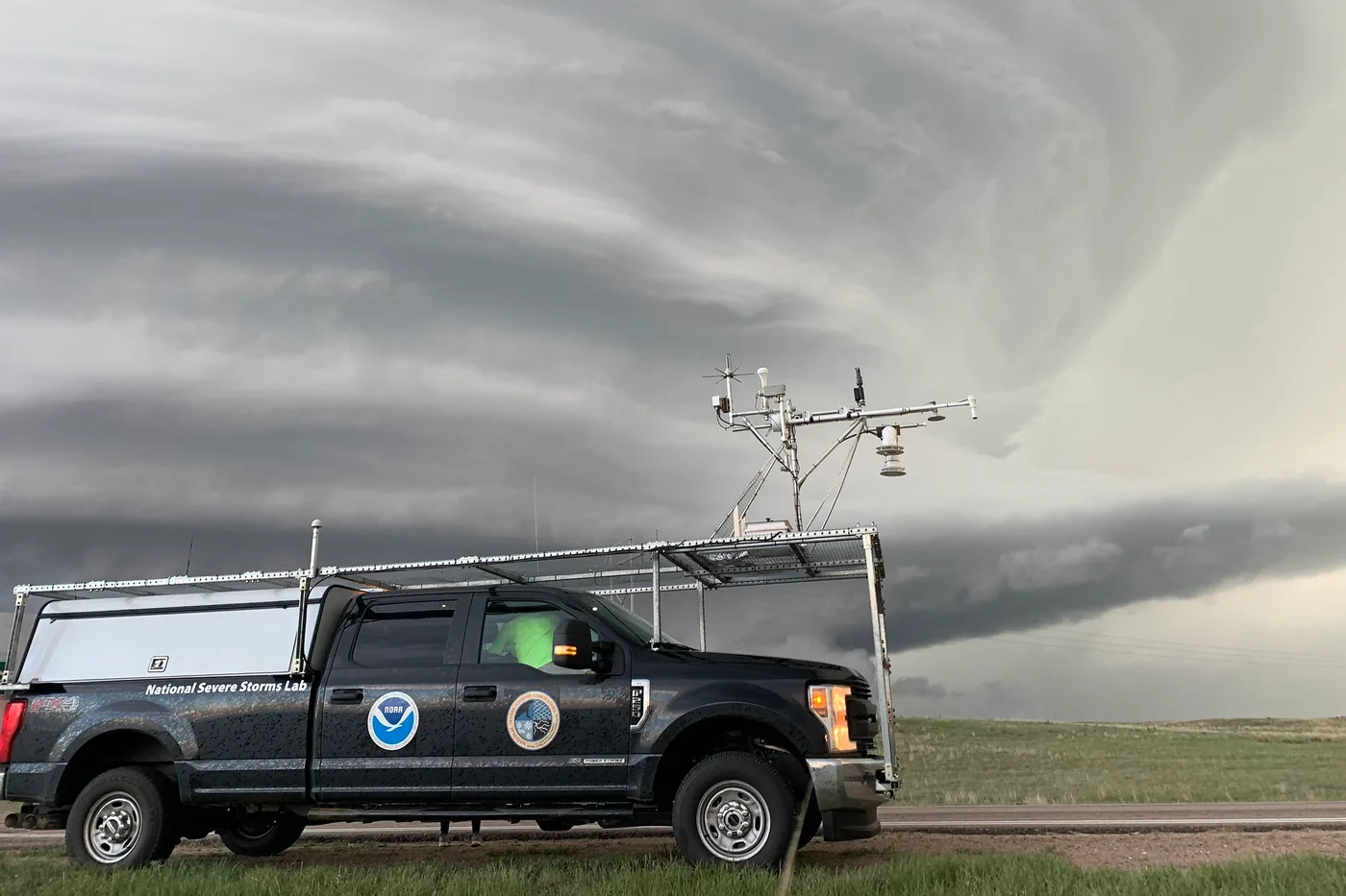 NOAA research truck with roof-mounted weather instruments parked beneath a sculpted storm cloud on the Plains