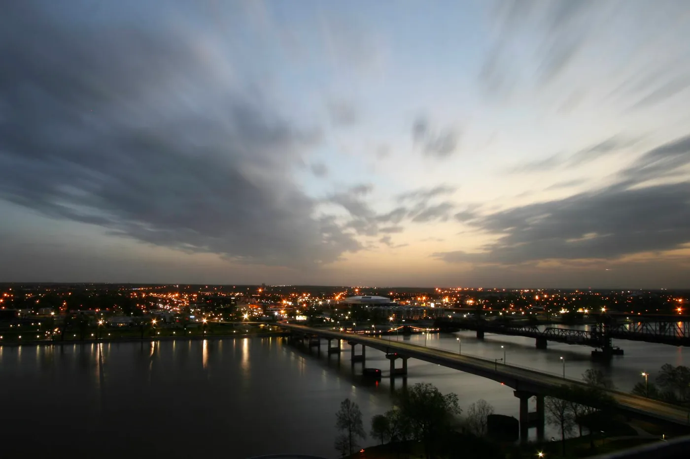 Clouds streaking over the swollen Arkansas River and the lights of Little Rock at dawn