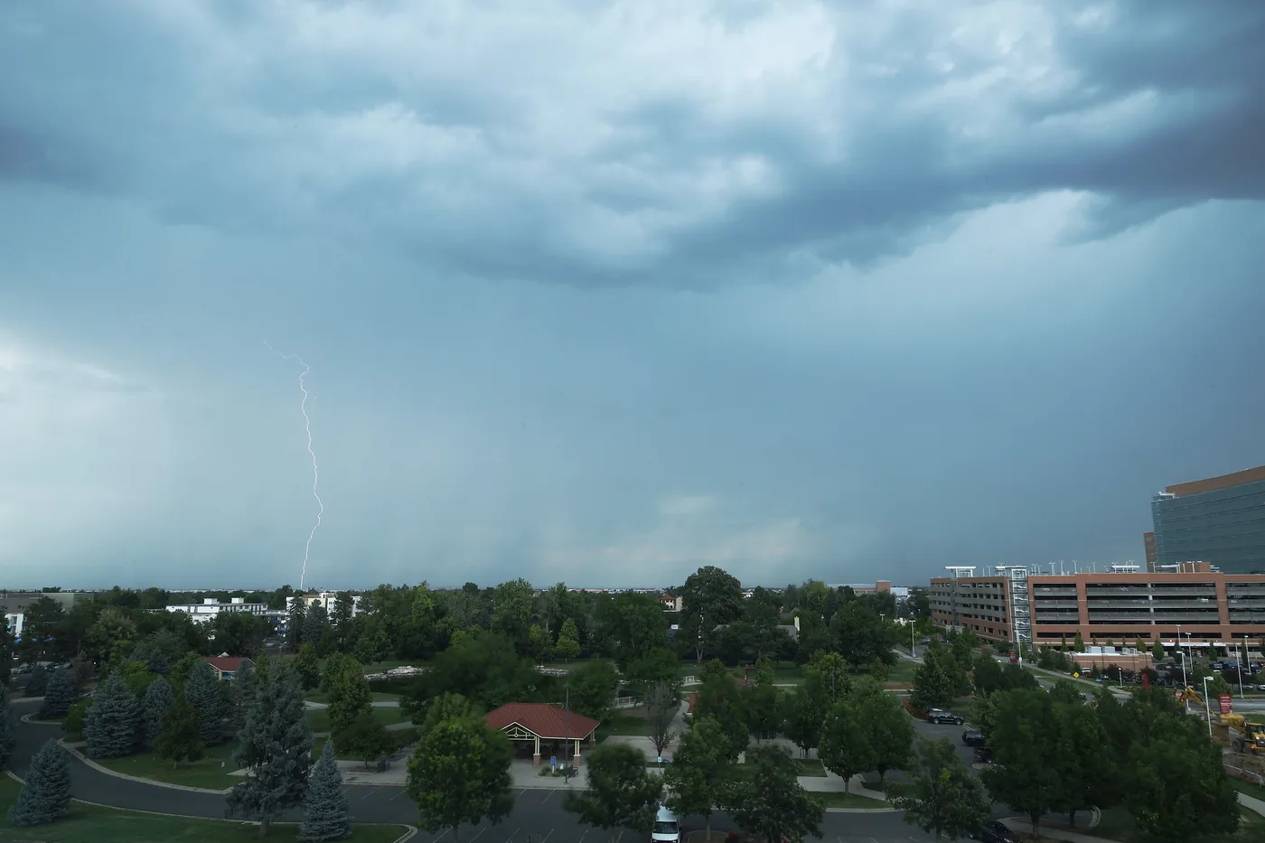 Lightning and a dark rain shaft over trees and buildings in Aurora, Colorado