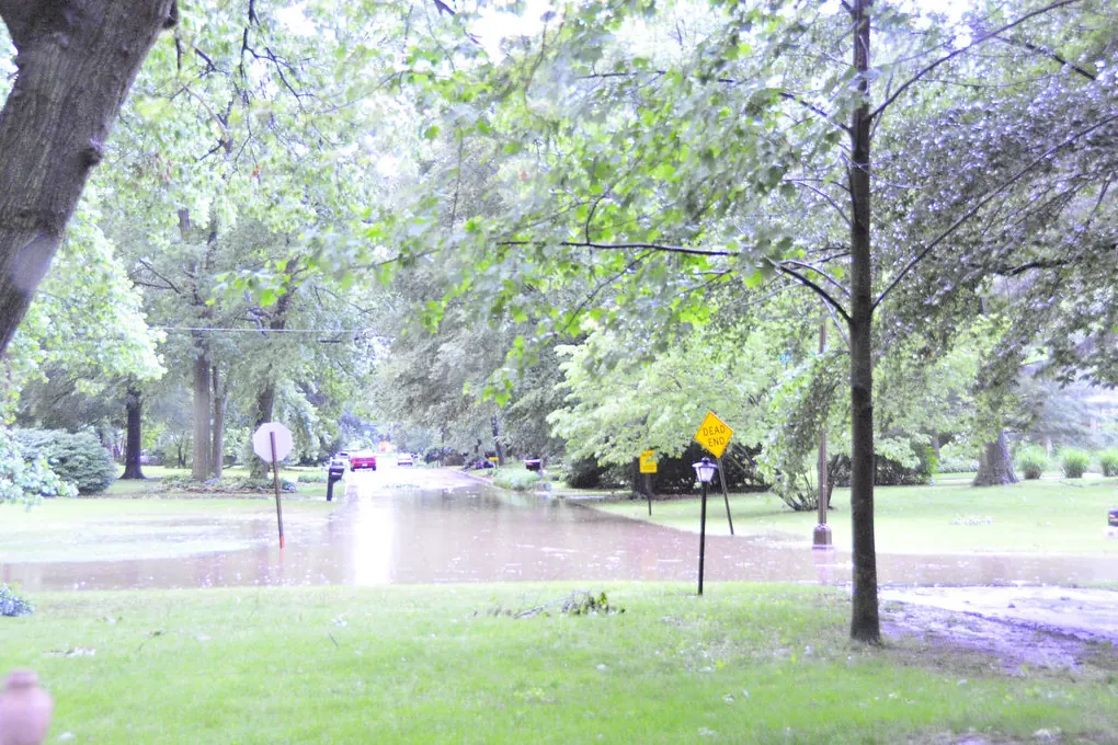 Flooded tree-lined street during a night thunderstorm in Indianapolis, lit by lightning during a long exposure