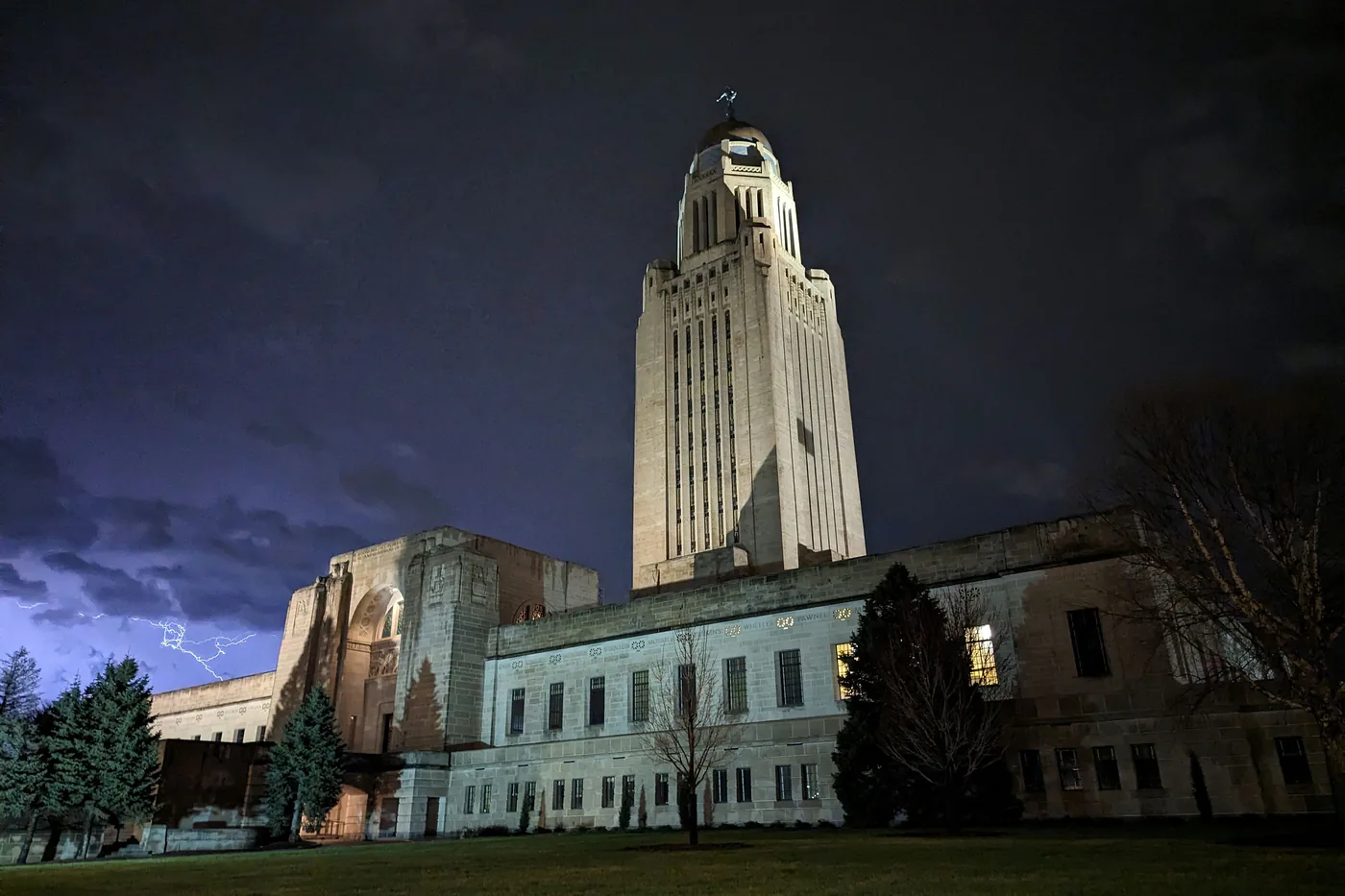 Nebraska State Capitol tower in Lincoln lit at night under a stormy sky