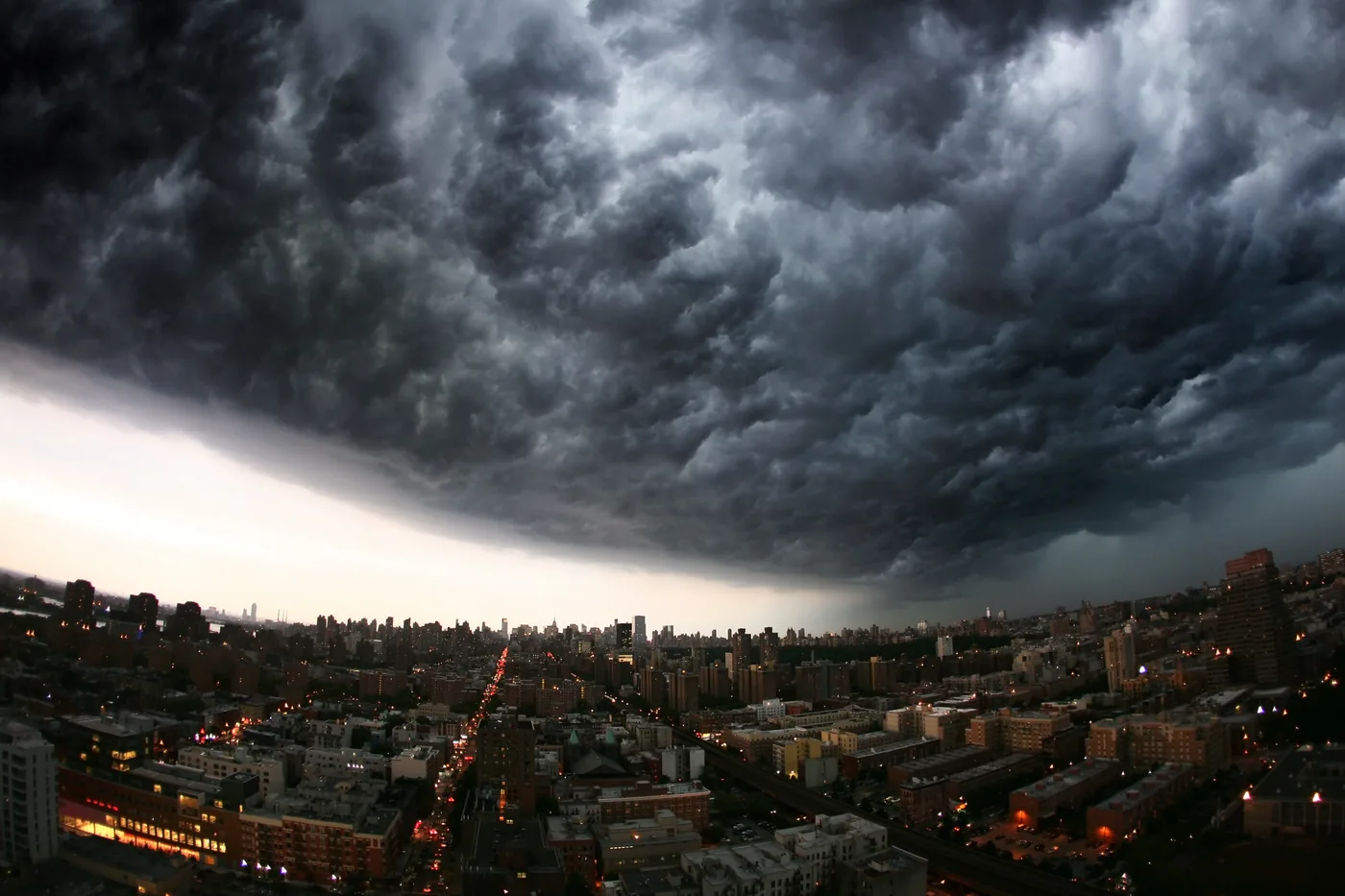 Dark, churning storm clouds rolling over the lights of New York City at dusk