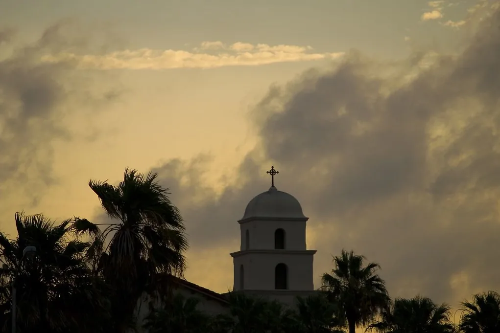 Bell tower of the Episcopal Church of the Good Shepherd and palm trees silhouetted against clearing storm clouds in Corpus Christi, Texas