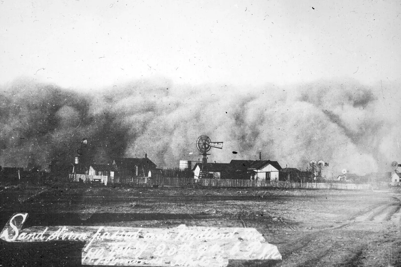 Wall of blowing sand passing over windmills and houses in Midland, Texas, on February 20, 1894, in a historic photo