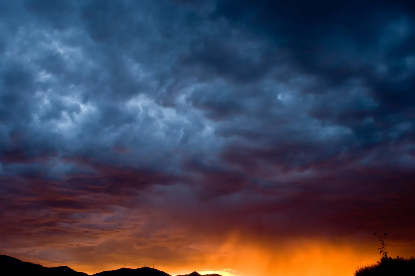 Dark storm clouds lit orange at sunset over the mountains, seen from West Jordan, Utah