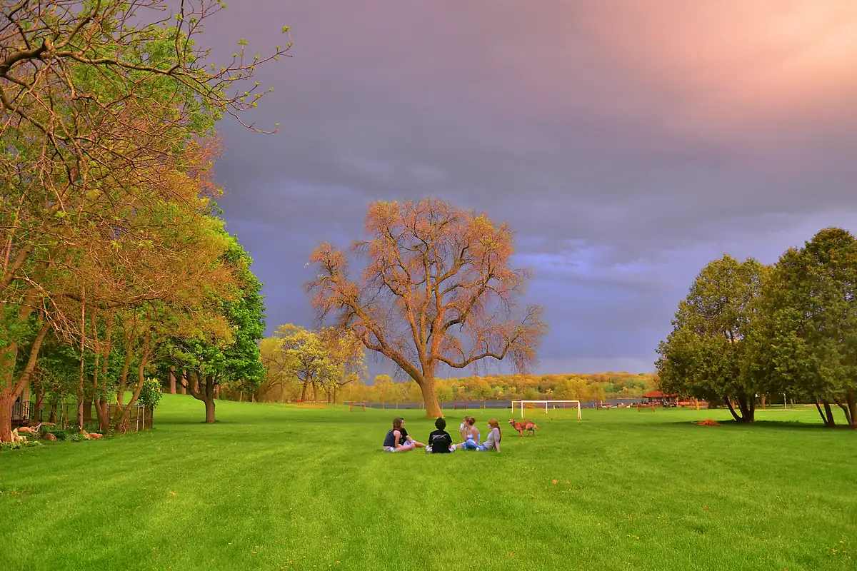 Spring thunderstorm approaching Wingra Park in Madison, Wisconsin, with people on the lawn under a darkening sky