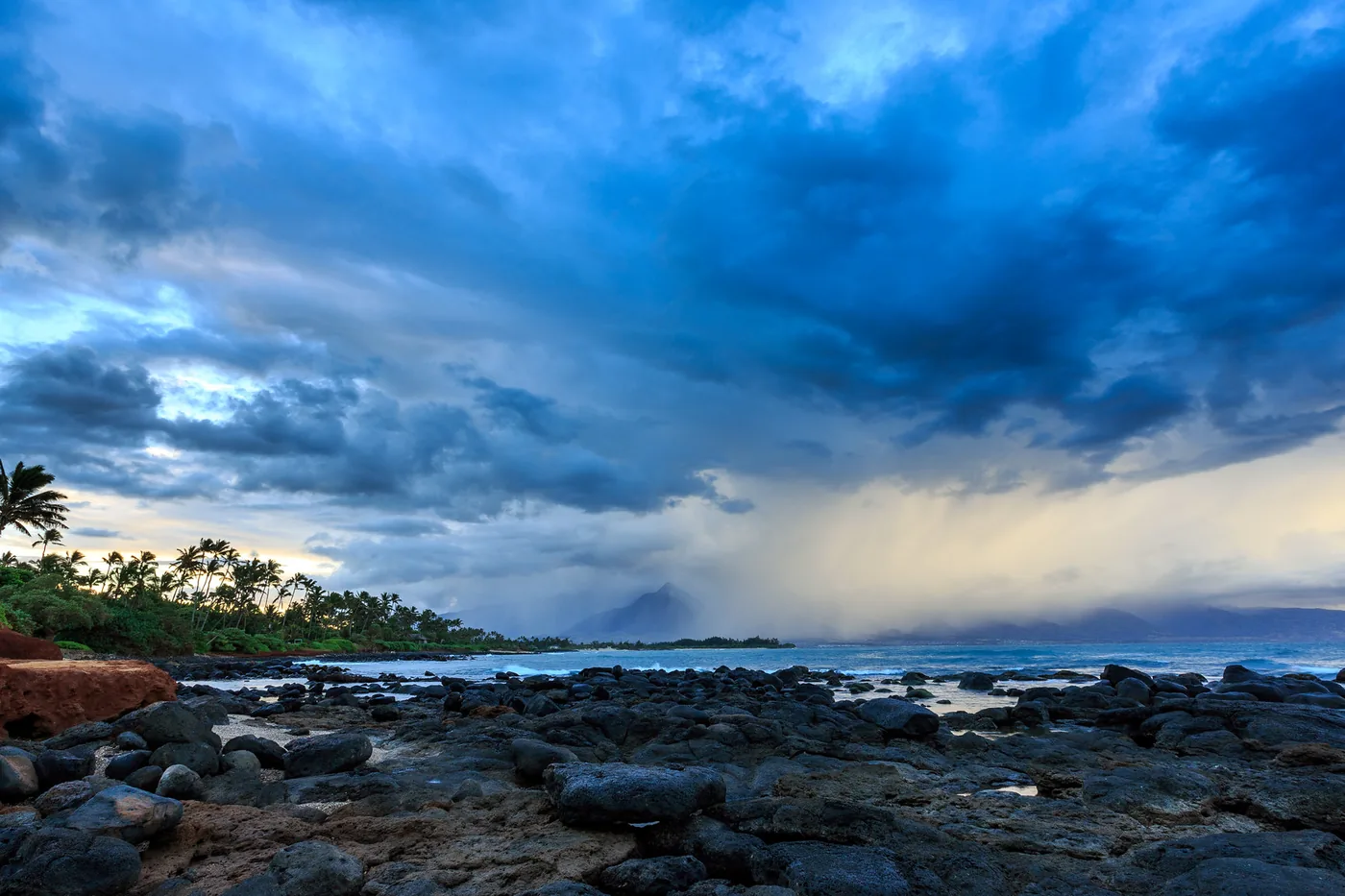 Dark storm clouds over the rocky shoreline and palms near Kahului, Maui, Hawaii