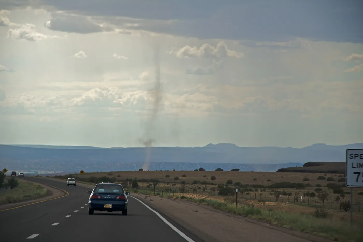 Dust devil spinning beside a highway under scattered thunderstorms in New Mexico