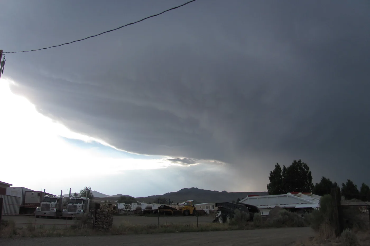 Dark thunderstorm base sweeping over ranch buildings and hills near Osino, Nevada